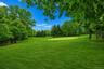 Expansive green space featuring a manicured lawn, surrounding mature deciduous and evergreen trees, and a putting green with a flagstick