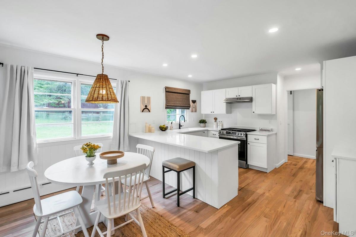 Open-concept kitchen featuring white shaker cabinetry, stainless steel appliances, a white countertop island with seating, a woven pendant light fixtu