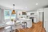 Open-concept kitchen featuring white shaker cabinetry, stainless steel appliances, a white countertop island with seating, a woven pendant light fixtu