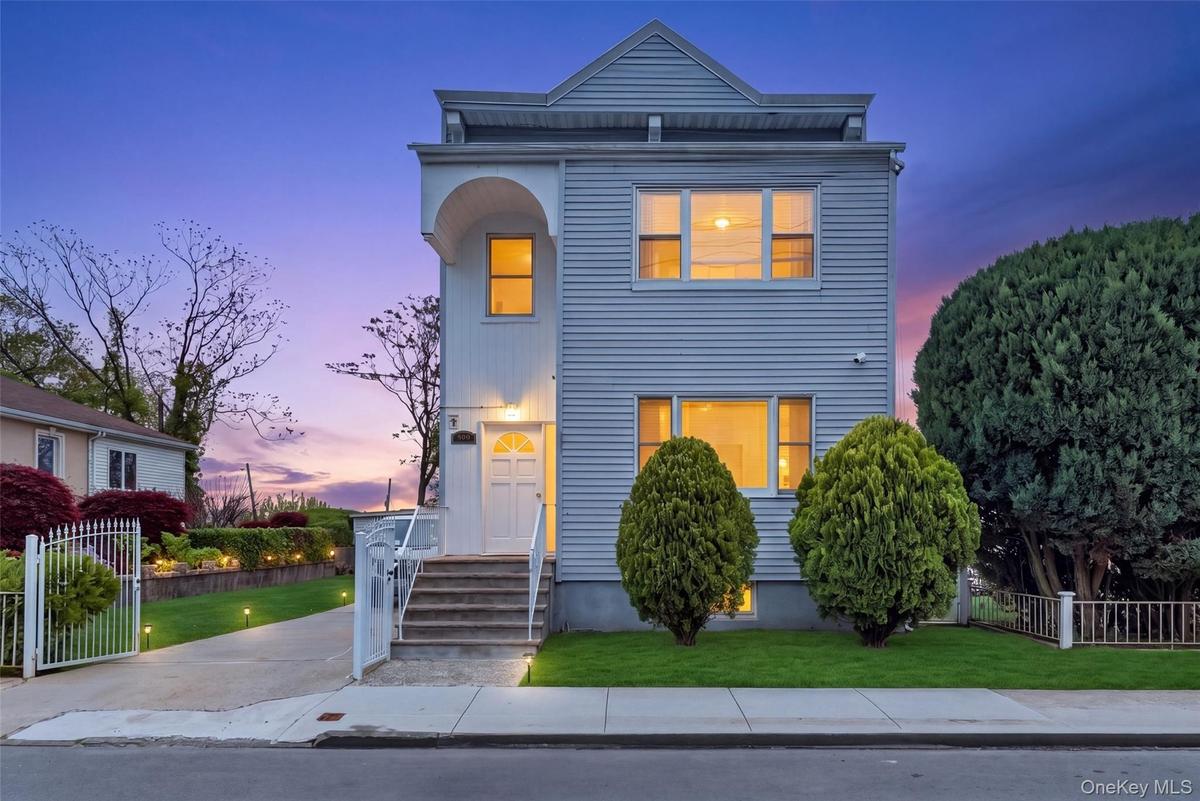 Two-story residence featuring light-colored siding, a prominent front entrance with a decorative door, and a concrete pathway leading to steps with wh