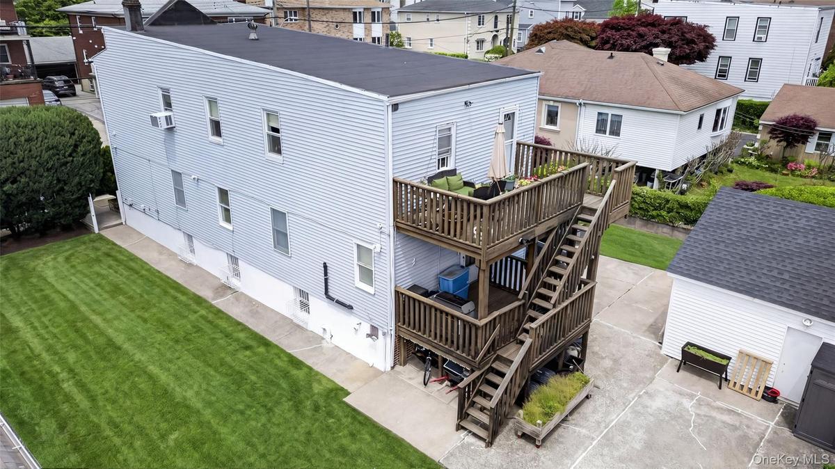 Three-story siding exterior featuring a two-level wood deck with stairs, a flat roof, and a cement driveway
