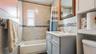 Bathroom featuring a light gray vanity with a white countertop, a white bathtub, and floor-to-ceiling tiled walls with a mosaic accent band
