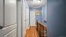 Hallway featuring wood-finish flooring, white panel doors, wood stair railing, and a flush mount ceiling light