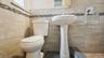 Bathroom featuring a white pedestal sink, toilet, and tiled walls with a decorative mosaic accent band