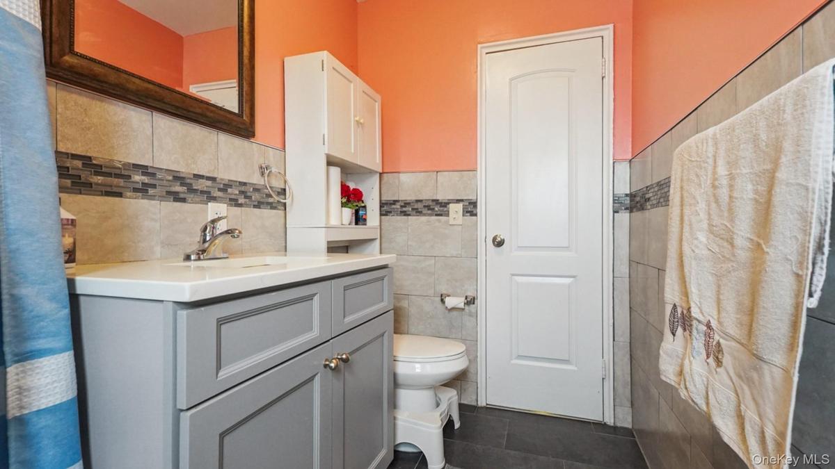 Bathroom featuring a gray vanity with a white countertop, tiled walls with a decorative mosaic accent, dark tile flooring, and a white paneled door