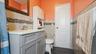 Bathroom featuring a gray vanity with a white countertop, tiled walls with a decorative mosaic accent, dark tile flooring, and a white paneled door