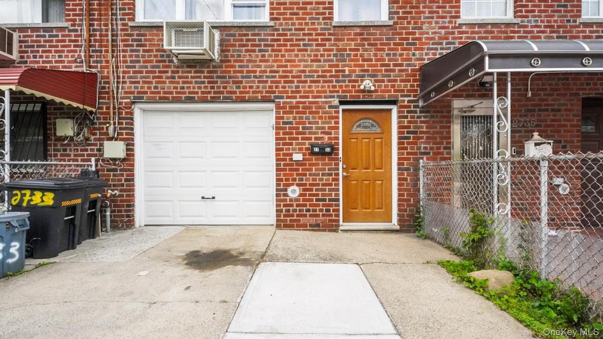 Brick facade featuring a panel garage door, light wood-finish entry door, and a concrete driveway