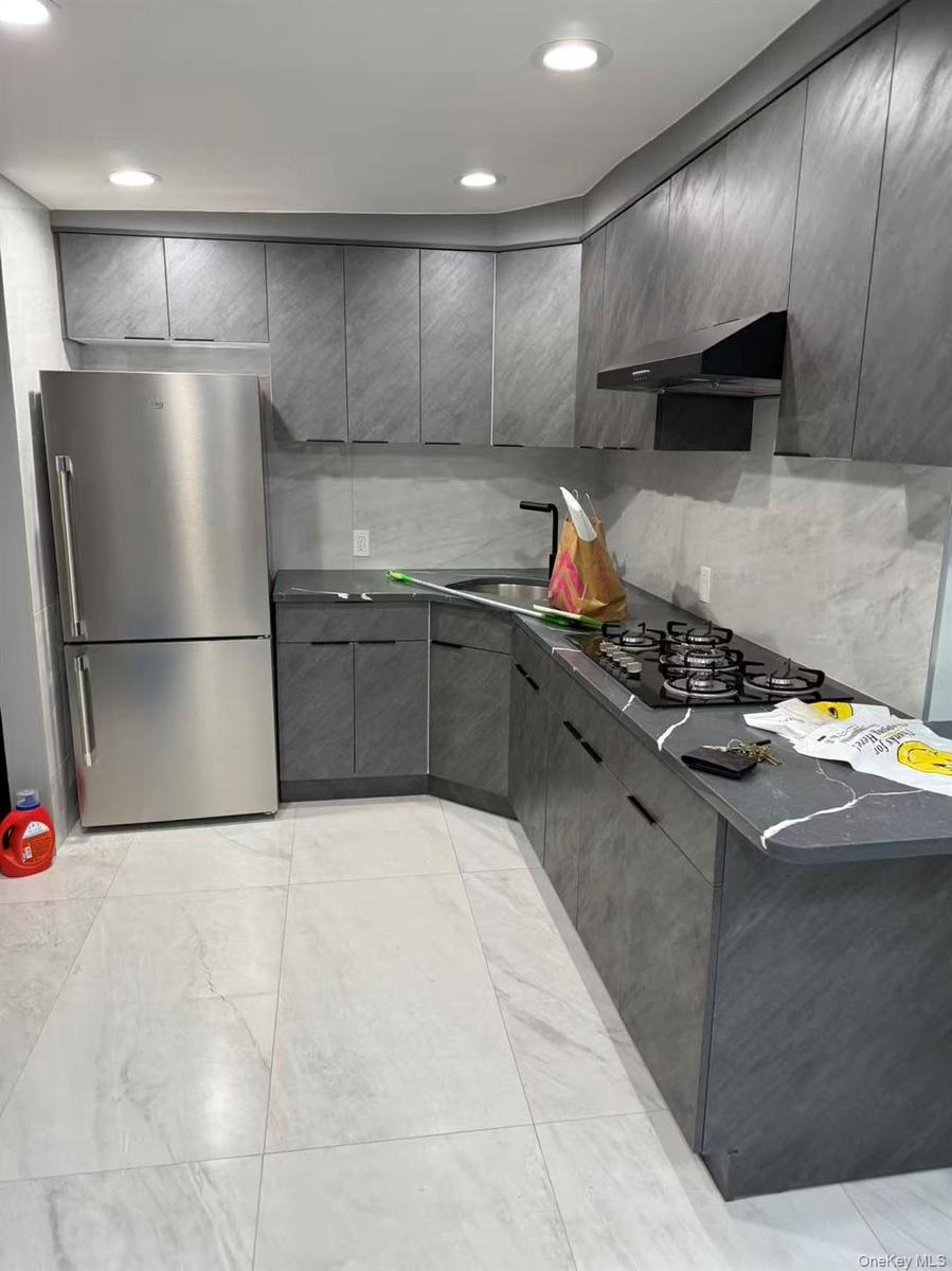Kitchen with dark countertops, gray cabinetry, freestanding refrigerator, tasteful backsplash, and under cabinet range hood