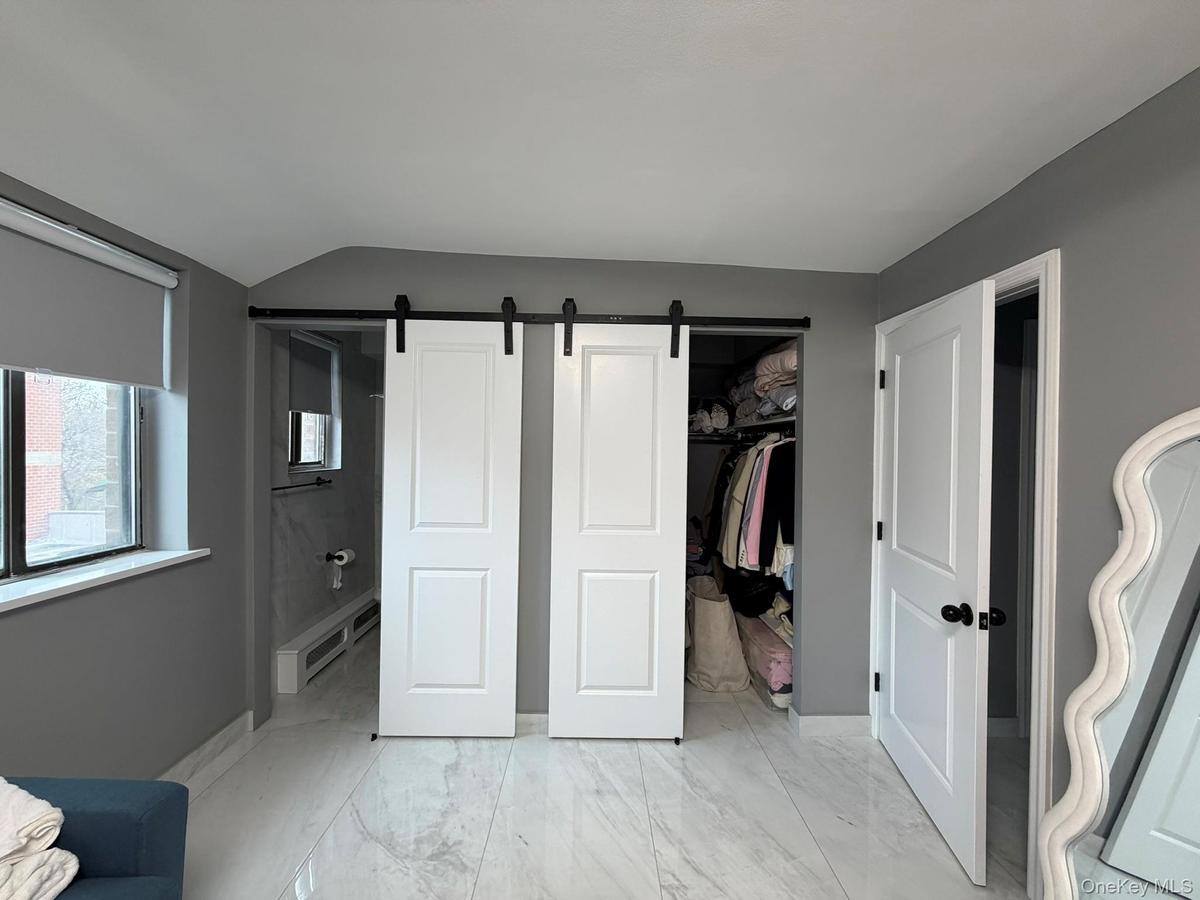 Bedroom with a barn door, light marble finish flooring, ensuite bathroom, a spacious closet, and a baseboard heating unit