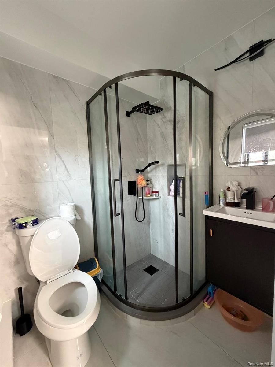 Bathroom featuring tile walls, vanity, a marble finish shower, and tile patterned floors