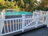Expansive outdoor deck featuring an above-ground pool, composite decking, white picket railing, and a coordinating gate
