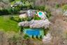 Aerial perspective showcasing a comprehensive property layout with a tennis court, swimming pool, extensive green lawns, mature trees, and a stone-cla