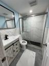 Modern basement bathroom featuring a glass enclosed shower with black hexagonal tile flooring and white marbled wall tile