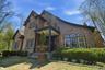 Shingle-sided exterior featuring an upper-level balcony, covered front entry with columns, multiple arched window sets, and a stone chimney