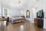 Spacious bedroom featuring vaulted ceilings, wood-finish flooring, two large windows, an overhead chandelier, and a white paneled door