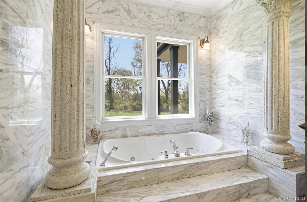 Integrated jetted tub set within a marble-clad platform with steps, flanked by decorative columns