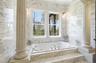 Integrated jetted tub set within a marble-clad platform with steps, flanked by decorative columns