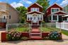 Red-sided residence featuring a front porch w white railing, a terraced front lawn, and a chain-link fence. digitally enhanced