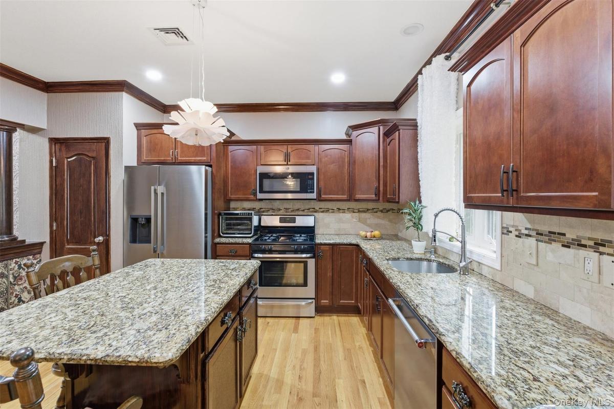 Kitchen featuring wood-finish cabinetry, granite countertops, stainless steel appliances, a center island, and wood-finish flooring