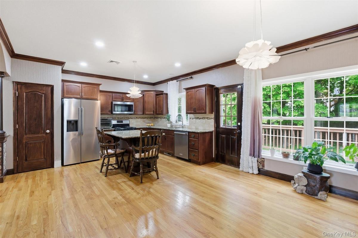Open-concept kitchen and living area featuring wood-finish flooring, dark wood cabinetry, stainless steel appliances, and a large window with exterior