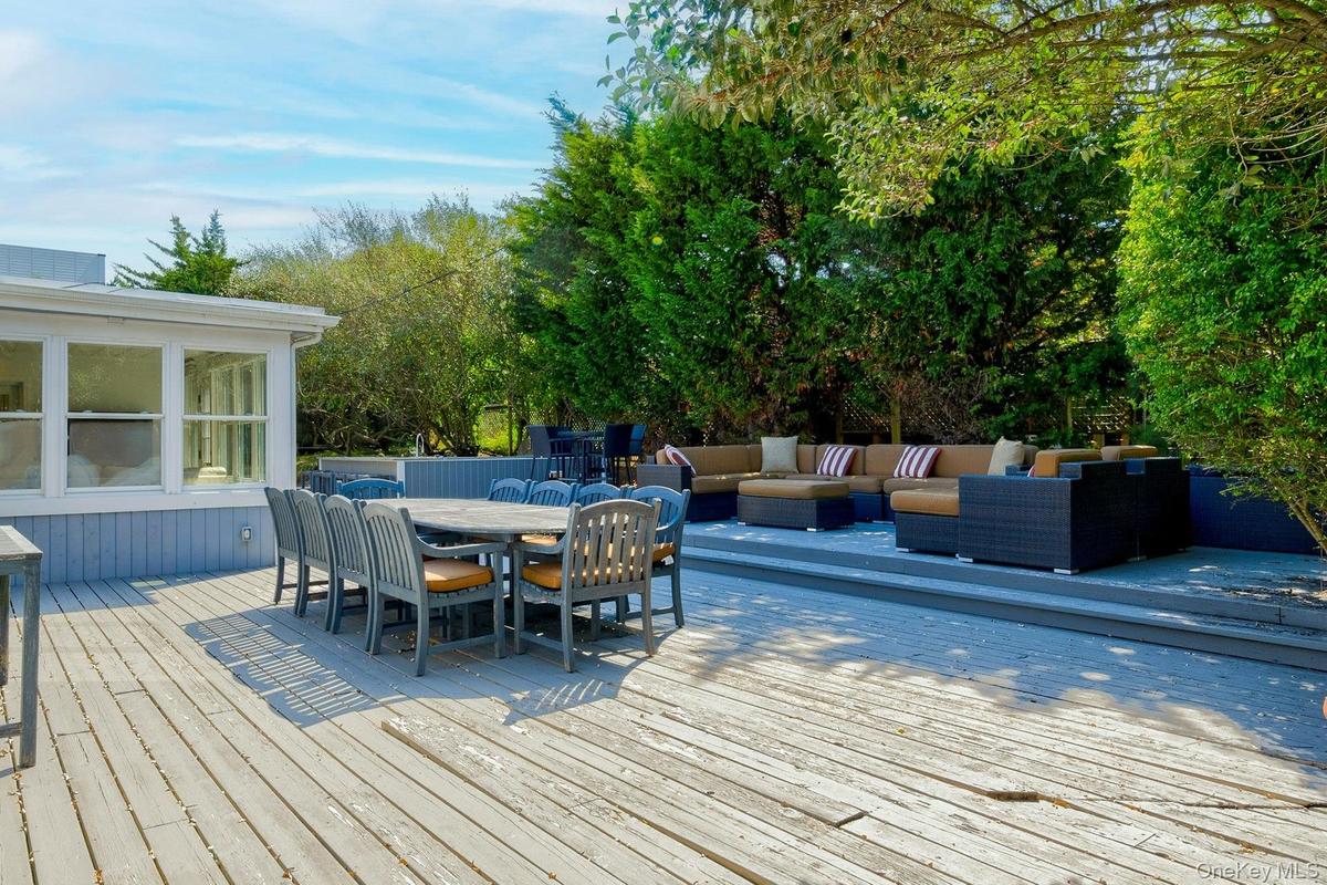 Multi-level wood deck featuring a dining area, a defined lounge space, and mature perimeter landscaping