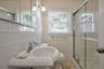 Bathroom featuring a pedestal sink, white tile walls, a sliding glass shower enclosure, and two windows with blinds
