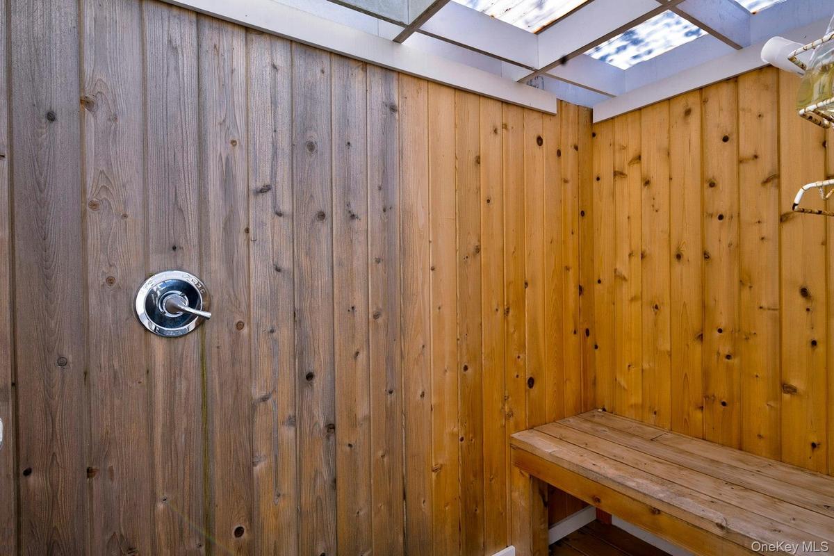 Wood-paneled outdoor shower featuring a built-in wooden bench and a chrome shower fixture
