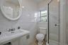 Bathroom featuring a pedestal sink, oval framed mirror, tiled walls, and a glass-enclosed shower