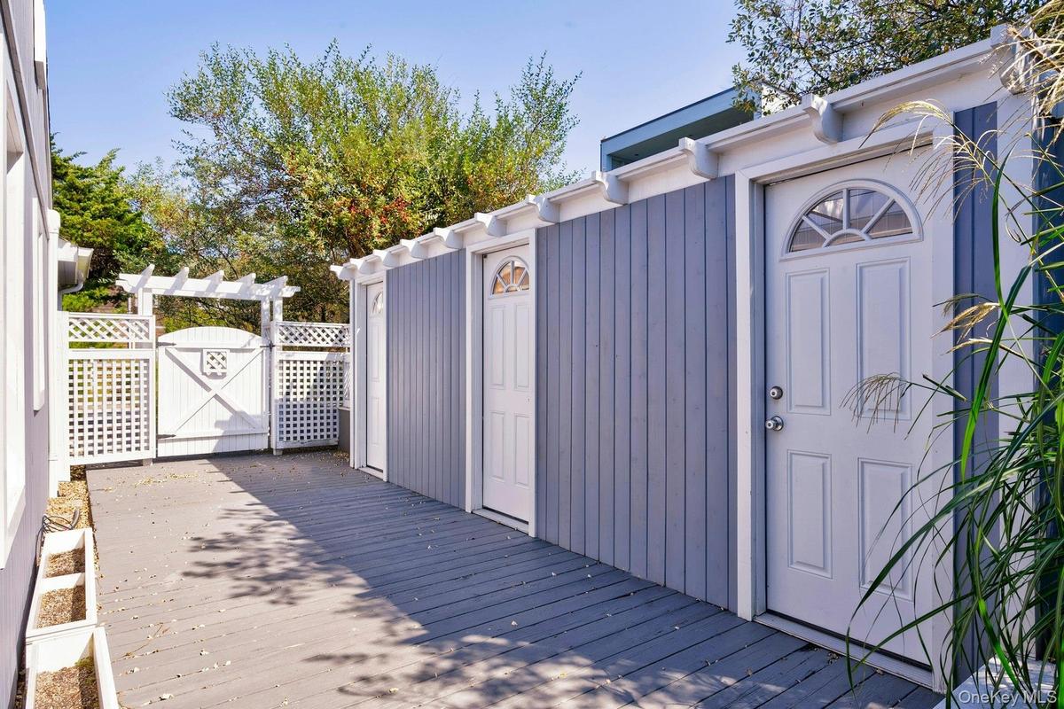 Exterior space featuring gray wood-finish decking, vertical siding in a muted blue hue, and multiple white paneled doors with arched transom windows