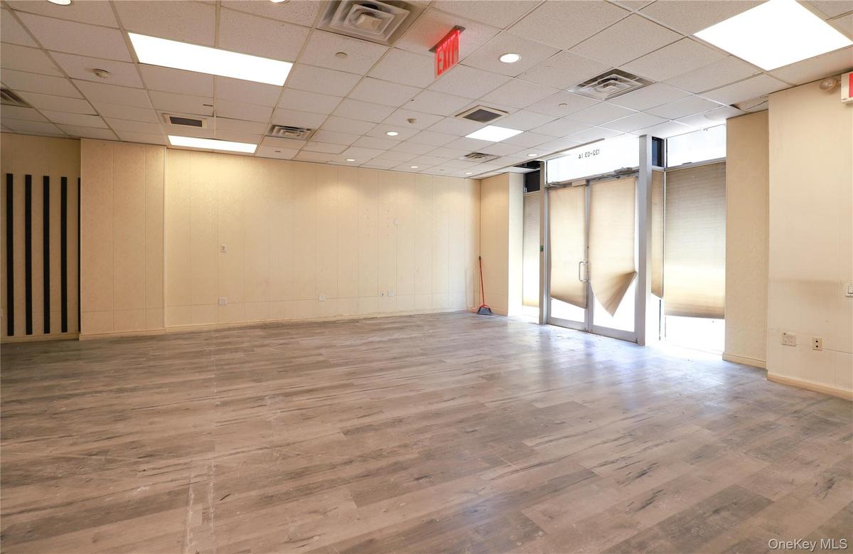 Expansive interior space featuring wood-finish flooring, drop ceiling with recessed lighting, and large storefront windows with roller shades