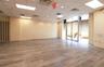 Expansive interior space featuring wood-finish flooring, drop ceiling with recessed lighting, and large storefront windows with roller shades