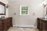 Dual dark wood vanities featuring integrated sinks and black countertops, bronze wall sconces, and a window