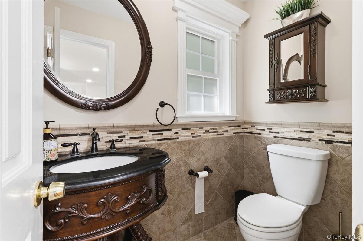 Powder room featuring a carved wood vanity with a black countertop, an oval framed mirror, an operable window with white trim, a decorative tile wains