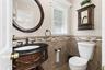 Powder room featuring a carved wood vanity with a black countertop, an oval framed mirror, an operable window with white trim, a decorative tile wains