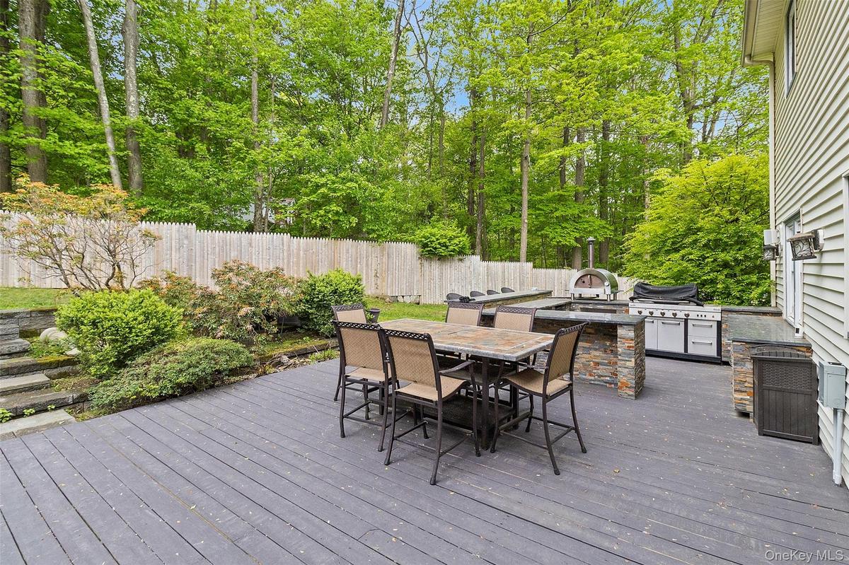 Spacious outdoor deck featuring an integrated outdoor kitchen with a built-in pizza oven, grill, and stone-clad base