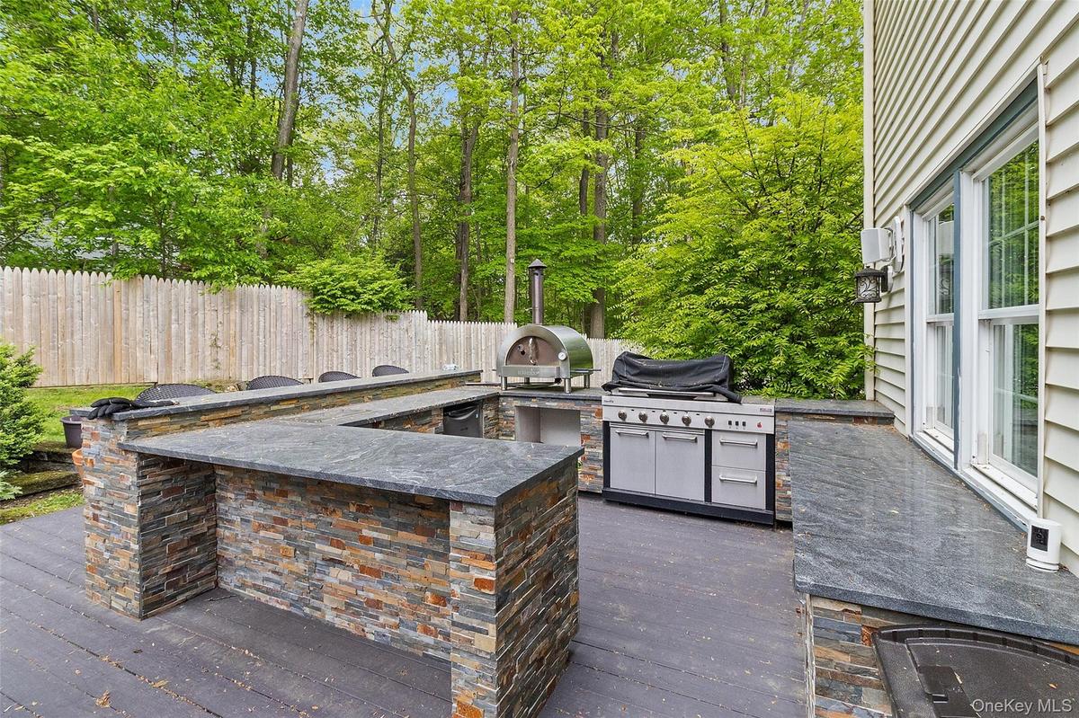 Outdoor kitchen featuring a U-shaped bar with stacked stone facade and dark countertops, a built-in grill, and an additional outdoor cooking appliance