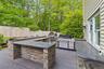 Outdoor kitchen featuring a U-shaped bar with stacked stone facade and dark countertops, a built-in grill, and an additional outdoor cooking appliance