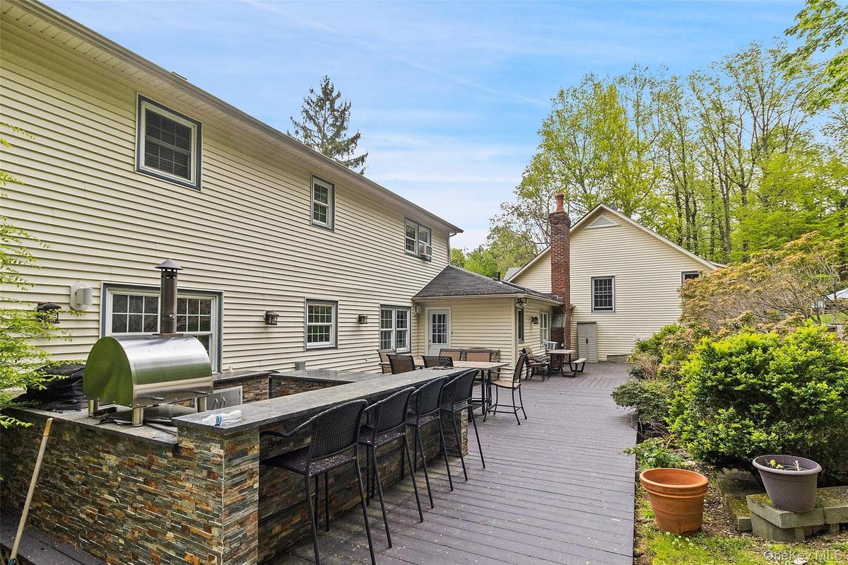 Expansive outdoor living area featuring a multi-level composite deck, built-in stone veneer outdoor kitchen with a stainless steel pizza oven, and a s