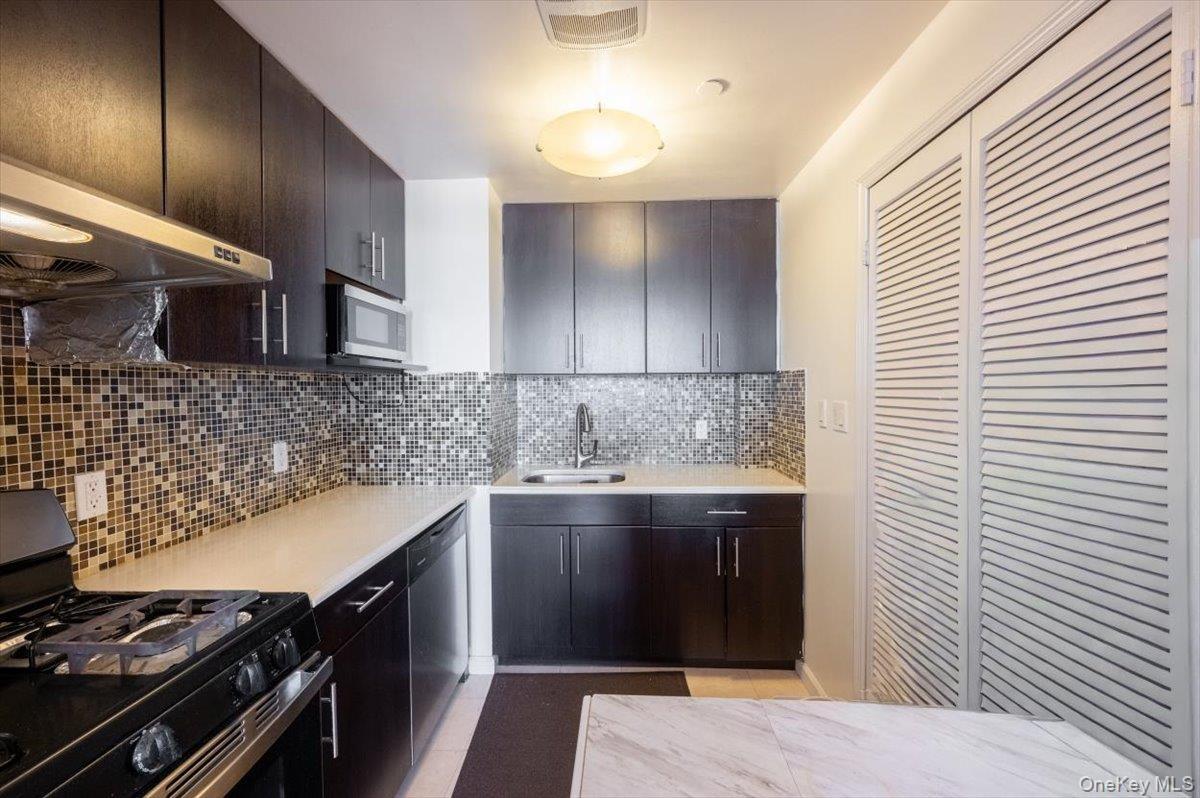 Kitchen with appliances with stainless steel finishes, decorative backsplash, light stone counters, and under cabinet range hood