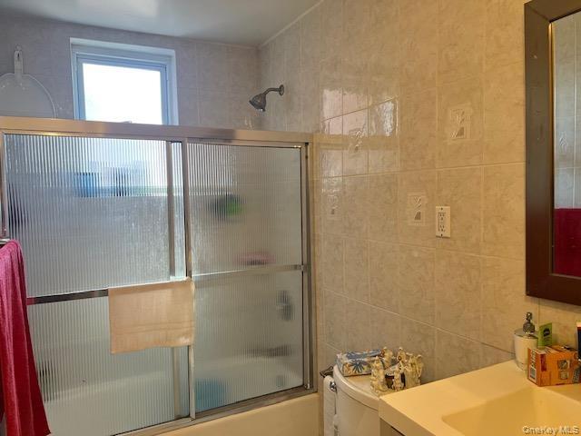 Bathroom featuring a full shower-tub combination with sliding frosted glass doors, a window, a wall-mounted showerhead, and tile walls