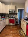 Kitchen featuring wood-finish flooring, light-toned cabinetry, stainless steel appliances, a dark tile backsplash, and granite countertops