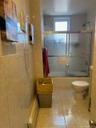 Bathroom featuring floor-to-ceiling tile, a bathtub with sliding glass doors, a window, and a standard toilet