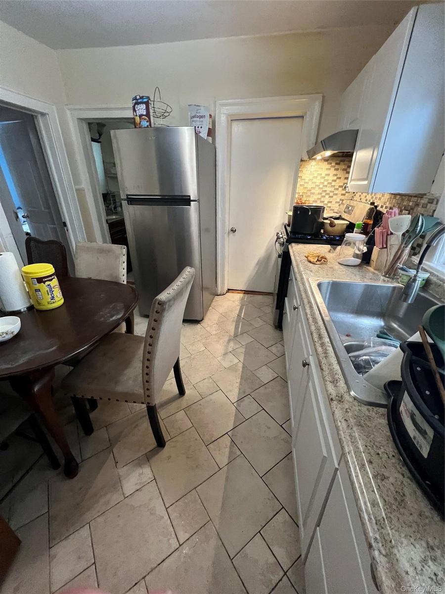 Kitchen featuring range, decorative backsplash, a sink, freestanding refrigerator, and white cabinets