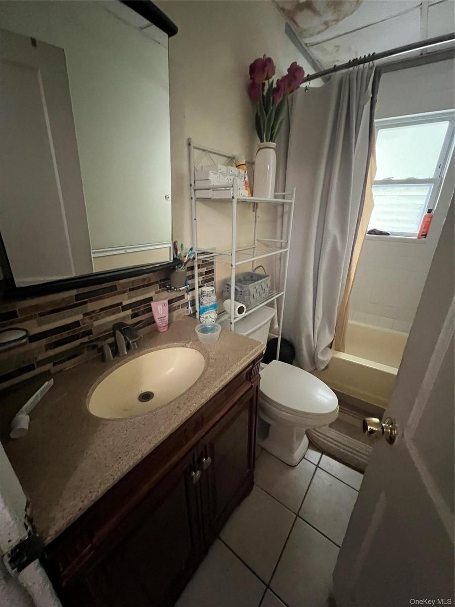 Bathroom with toilet, vanity, tasteful backsplash, shower / tub combo with curtain, and tile patterned flooring