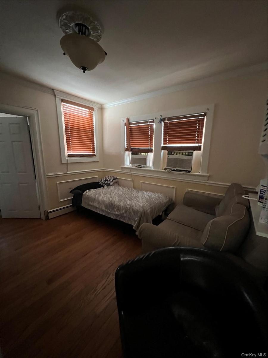 Bedroom featuring cooling unit, wood finished floors, crown molding, and a baseboard radiator