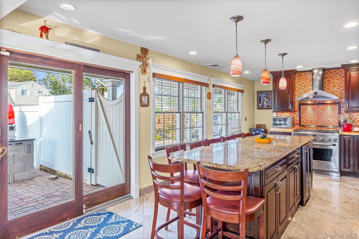 Kitchen with a breakfast bar, decorative backsplash, light stone counters, hanging light fixtures, and wall chimney exhaust hood