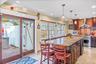 Kitchen with a breakfast bar, decorative backsplash, light stone counters, hanging light fixtures, and wall chimney exhaust hood
