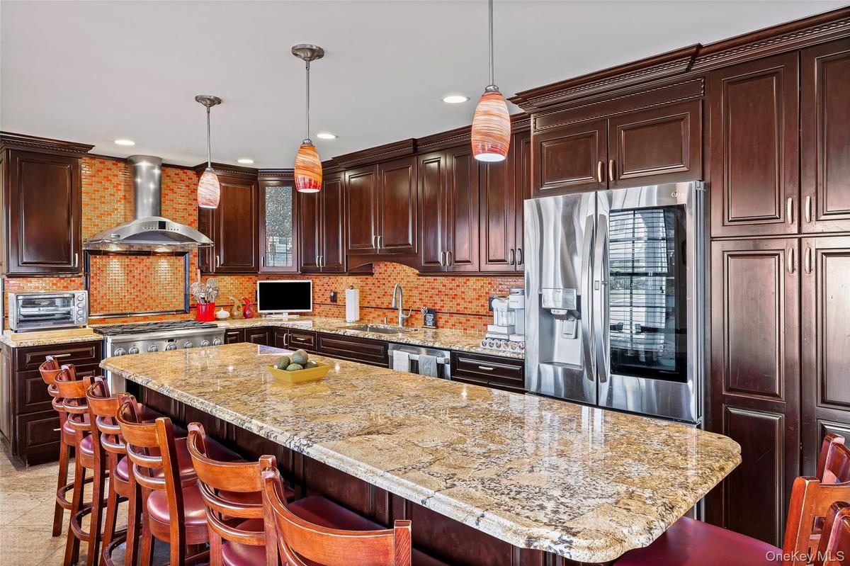 Kitchen with a breakfast bar area, dark brown cabinets, appliances with stainless steel finishes, wall chimney range hood, and recessed lighting