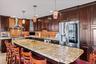 Kitchen with a breakfast bar area, dark brown cabinets, appliances with stainless steel finishes, wall chimney range hood, and recessed lighting