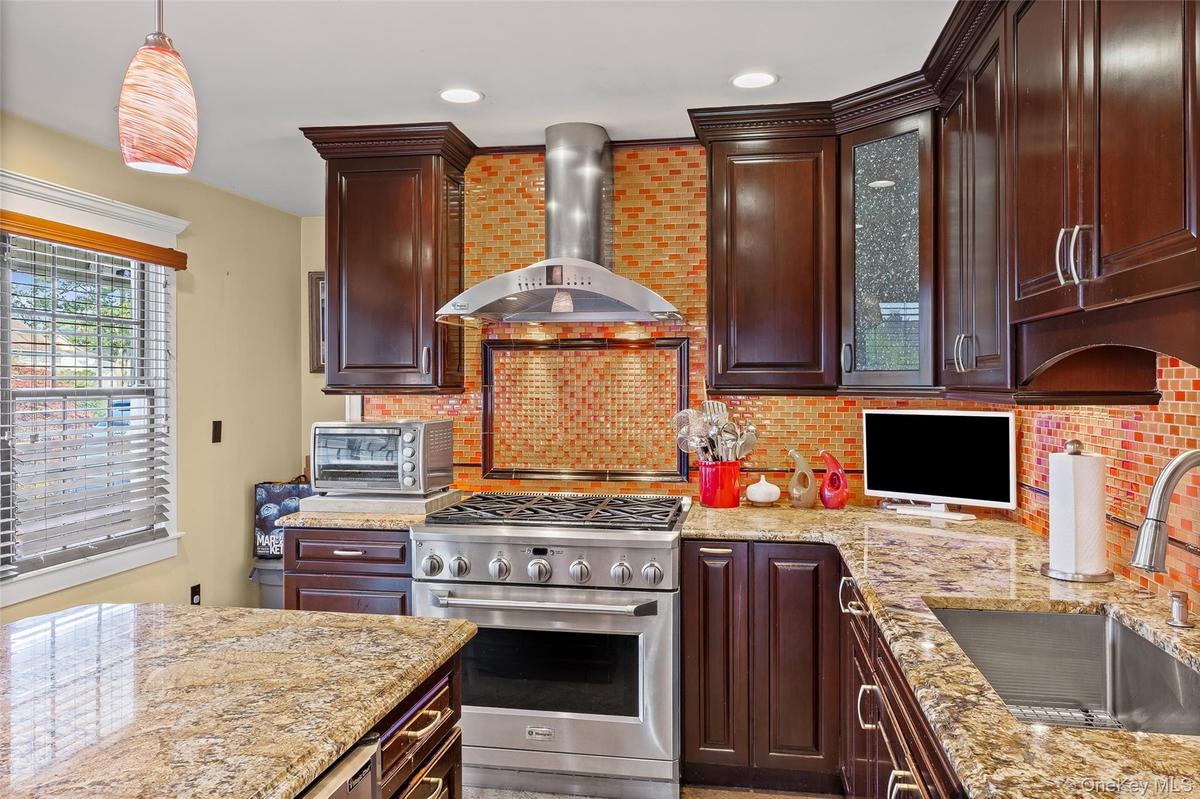 Kitchen with high end stainless steel range, wall chimney range hood, light stone countertops, decorative backsplash, and dark brown cabinetry